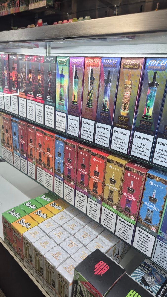 Rows of boxed disposable vapes on lit shelves, each carrying its nicotine warning label.