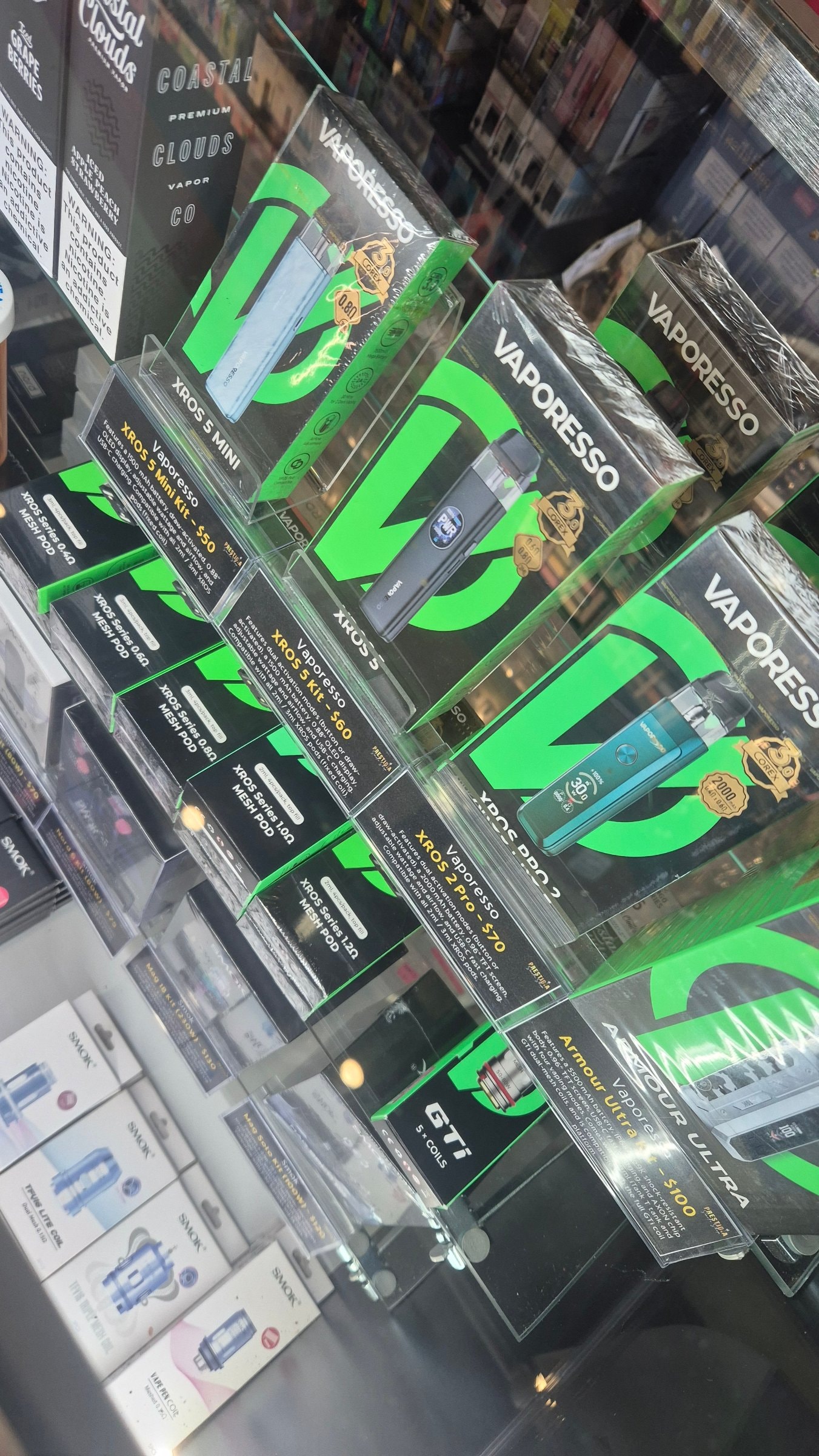 Pod systems and coils on a shelf wall, each with a handwritten price card.